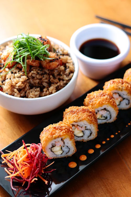 Close-up of Sushi on a Black Plate and a Bowl with a Rice Dish 