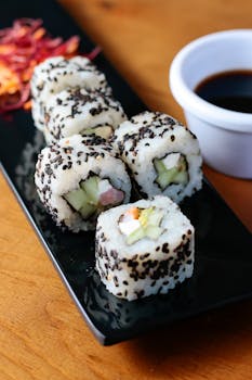 Close-up of sushi roll with black sesame seeds on a black plate, perfect for culinary themes.