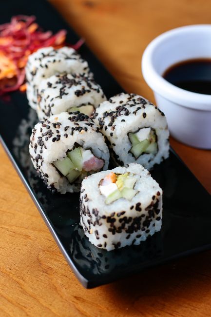 Fotomural Primer plano de un rollo de sushi con semillas de sésamo negro en un plato negro, perfecto para temas culinarios.
