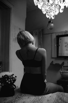 Artistic black and white photo of a woman in lingerie sitting with back view in a dimly lit room.