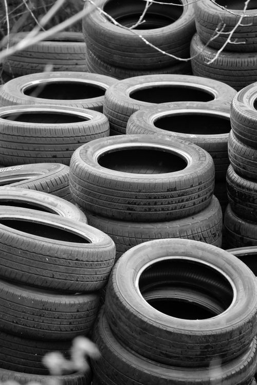 Free A vertical black and white photograph of stacked car tires in an outdoor setting. Stock Photo