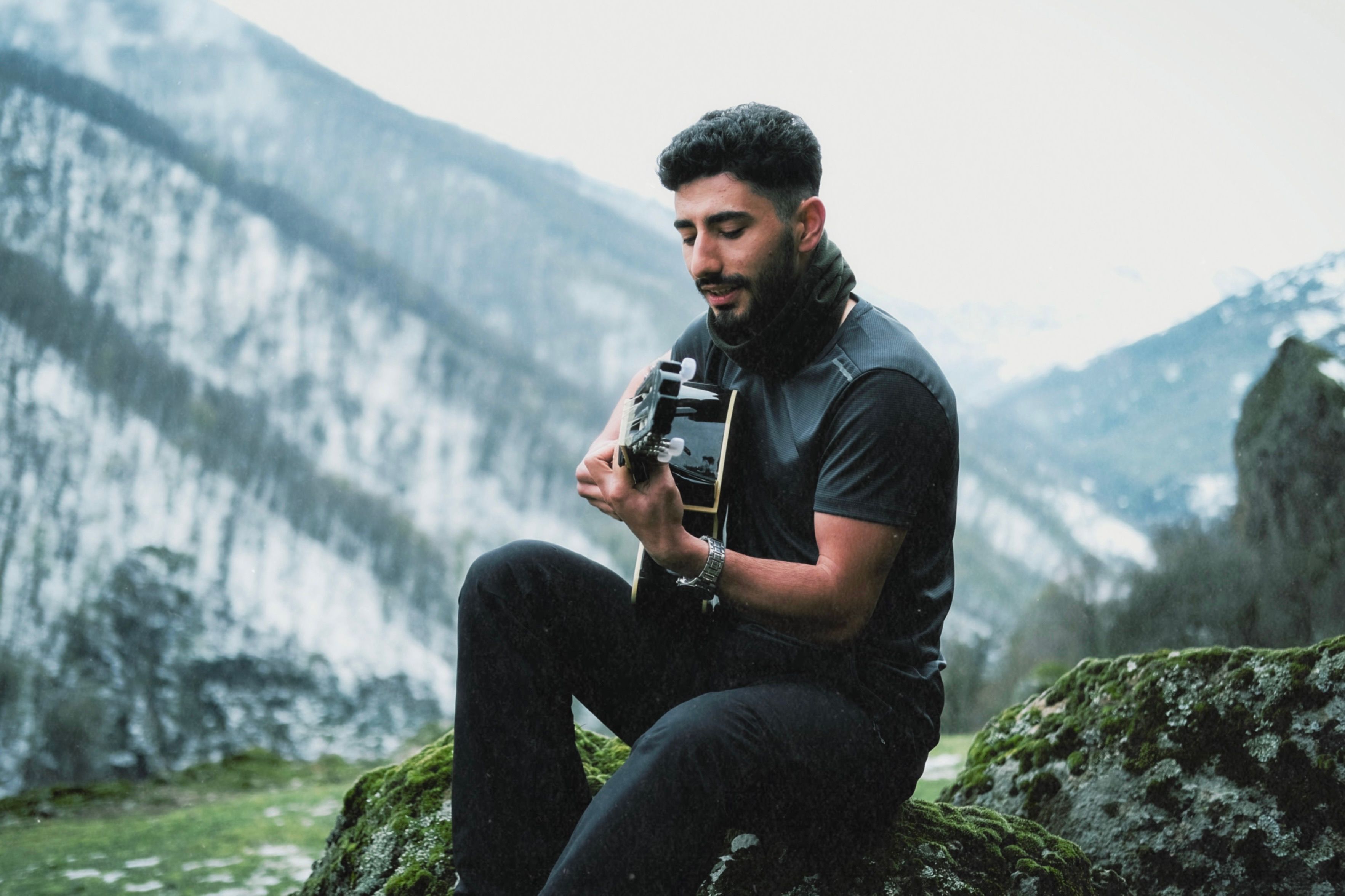 Man Sitting on the Rock in a Mountain Valley and Playing the Guitar ...