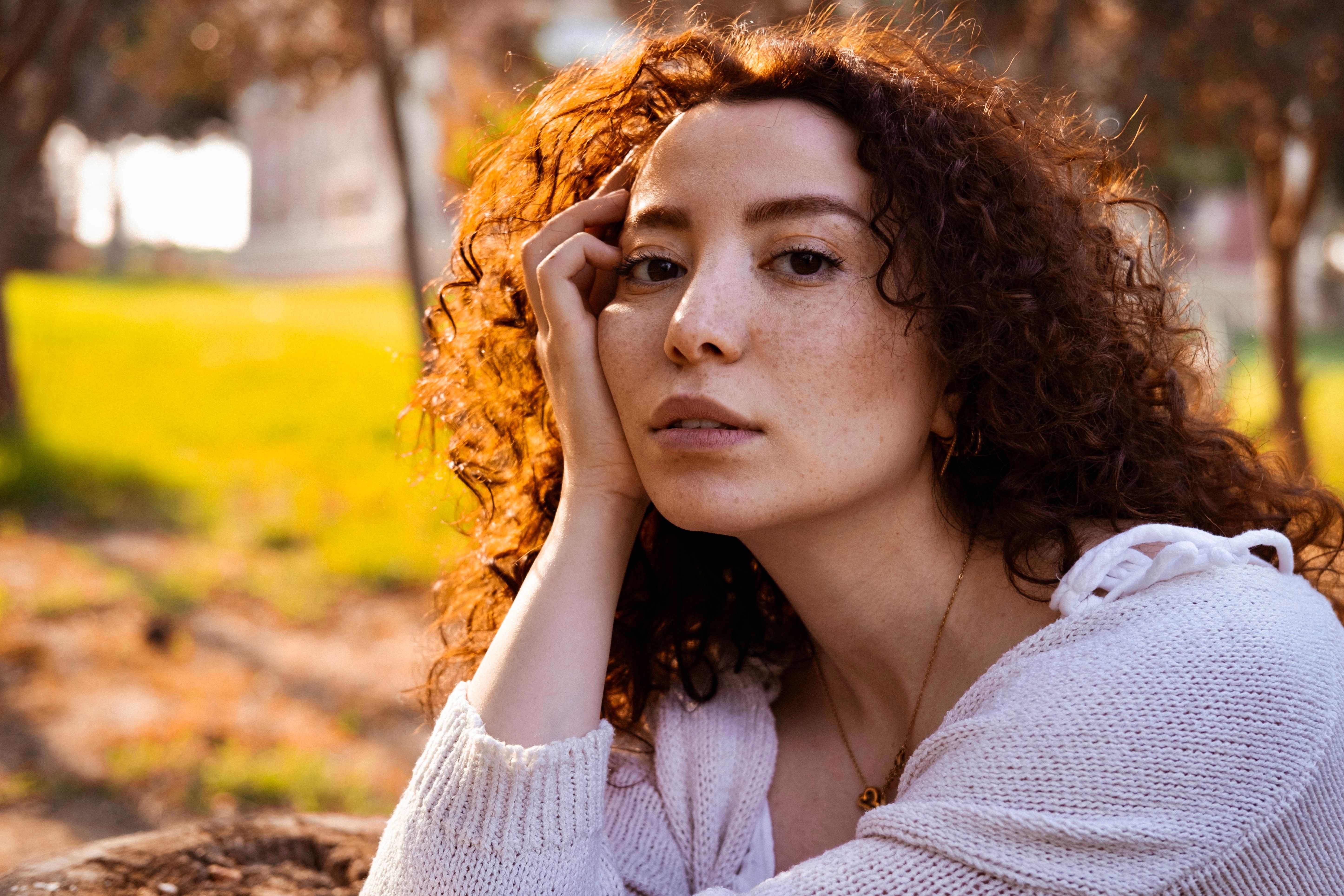 Portrait of a young woman with curly hair relaxing in a sunlit park setting.