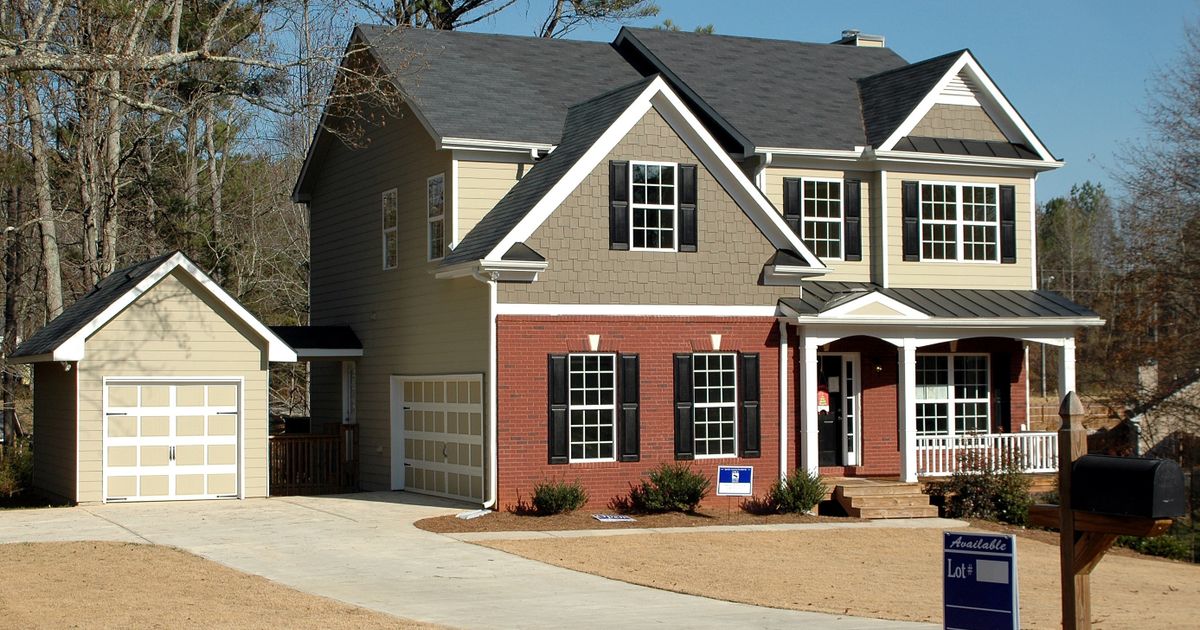 A newly finished two-story home with an attached garage and an "Available Lot" sign staked in the front yard.