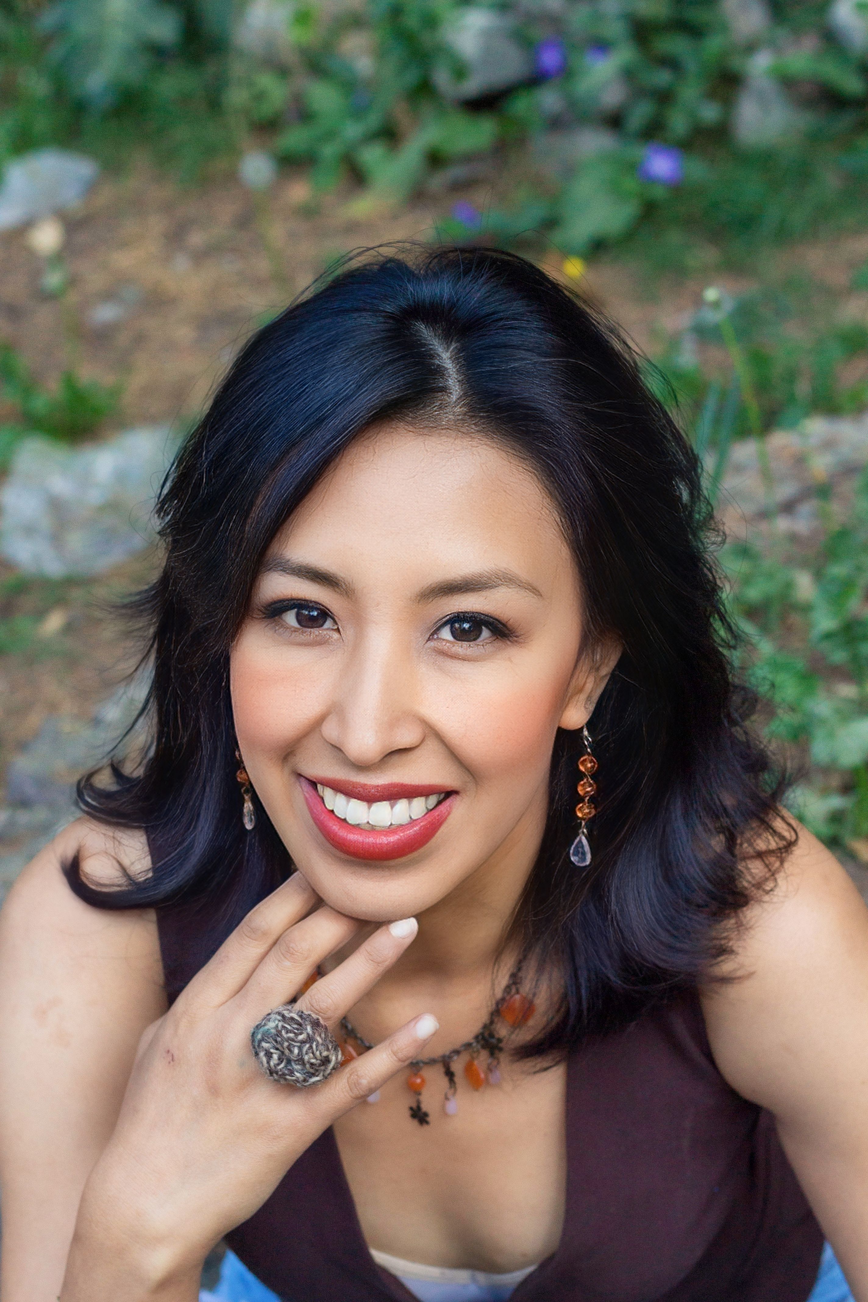 A cheerful woman with jewelry, smiling outside in natural surroundings.