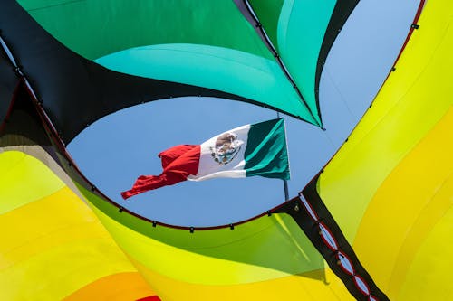 A Mexican Flag on the Flagpole seen between Colorful Fabric 