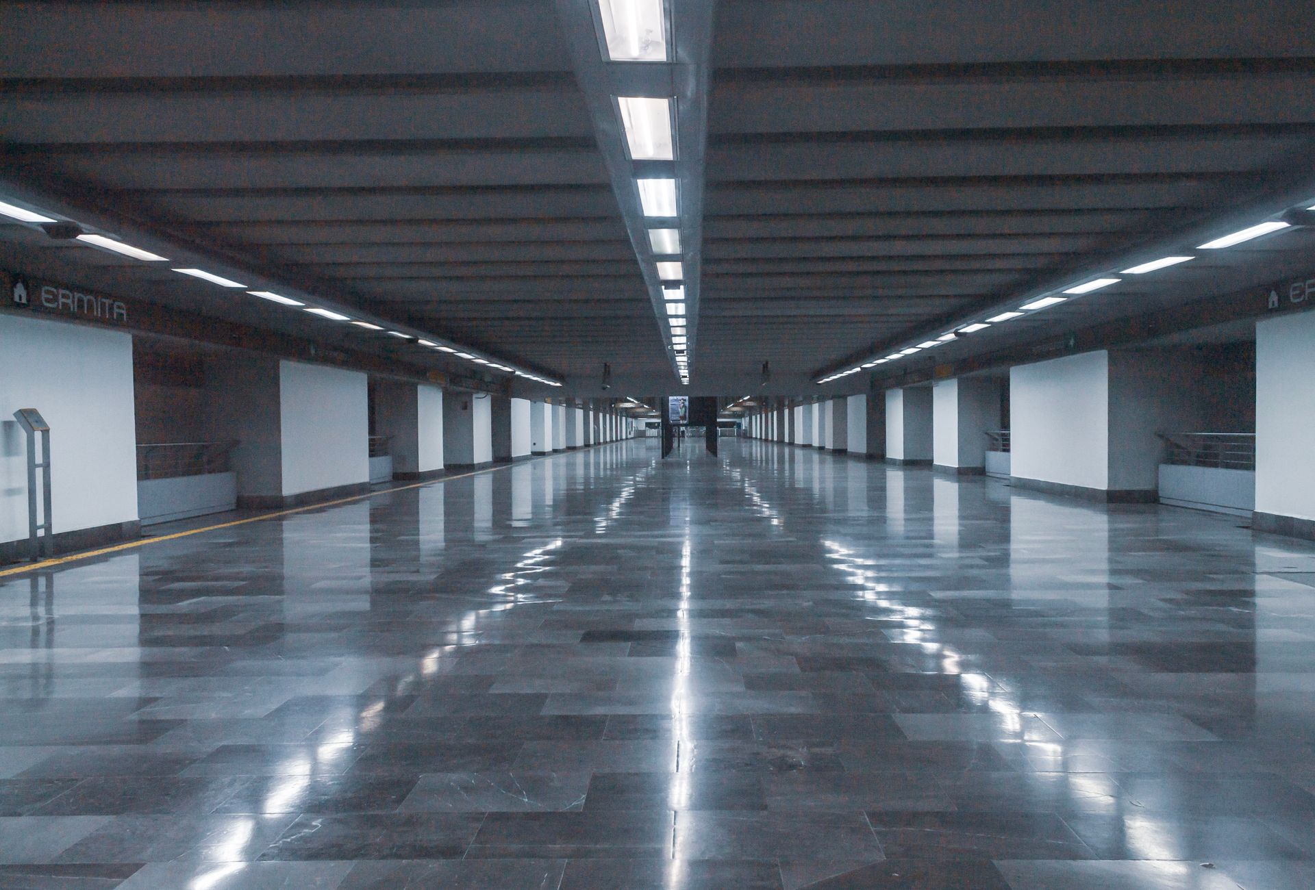 Empty modern underground metro station with reflective flooring and fluorescent lighting.