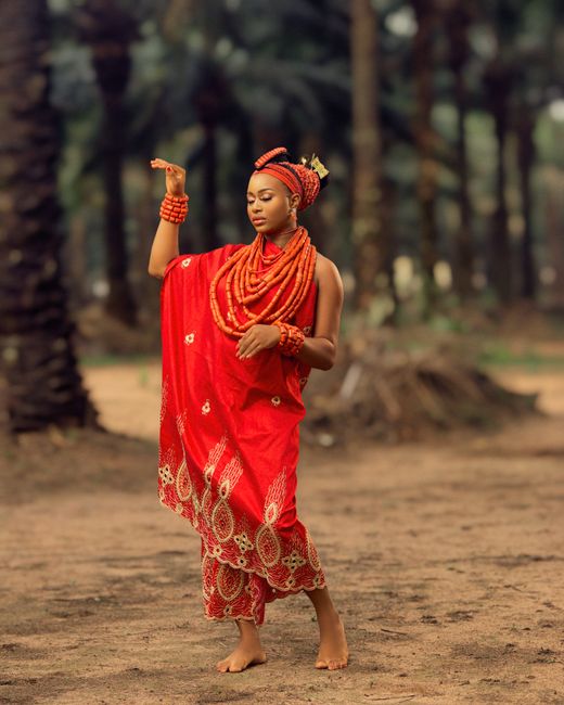 Elegant African woman posing in a vibrant red traditional dress outdoors.