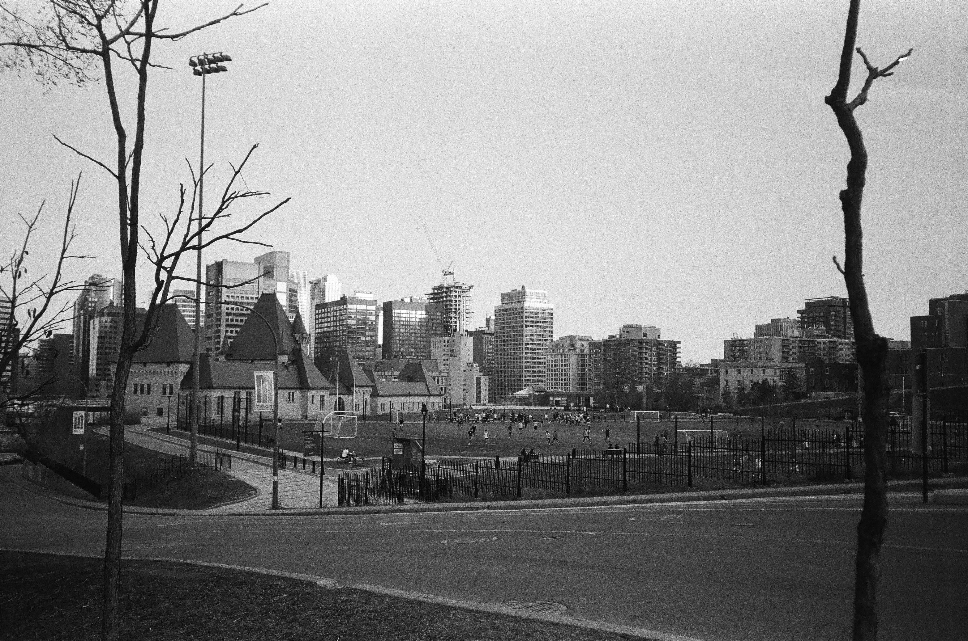 Urban landscape with a soccer field and skyline in black and white, people visible.