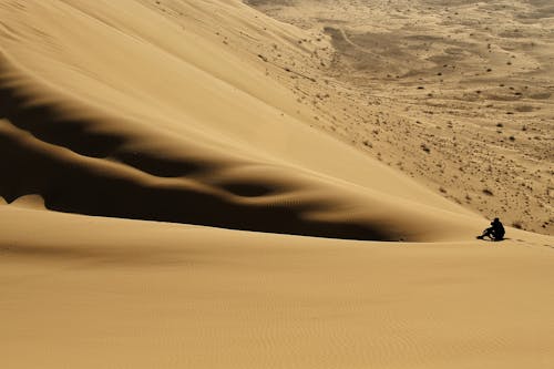 Silhouette of a Person Sitting on a Dune in a Desert 