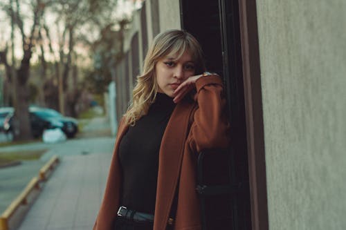 Young Woman in a Black Blouse and Brown Coat Standing next to a Wall 