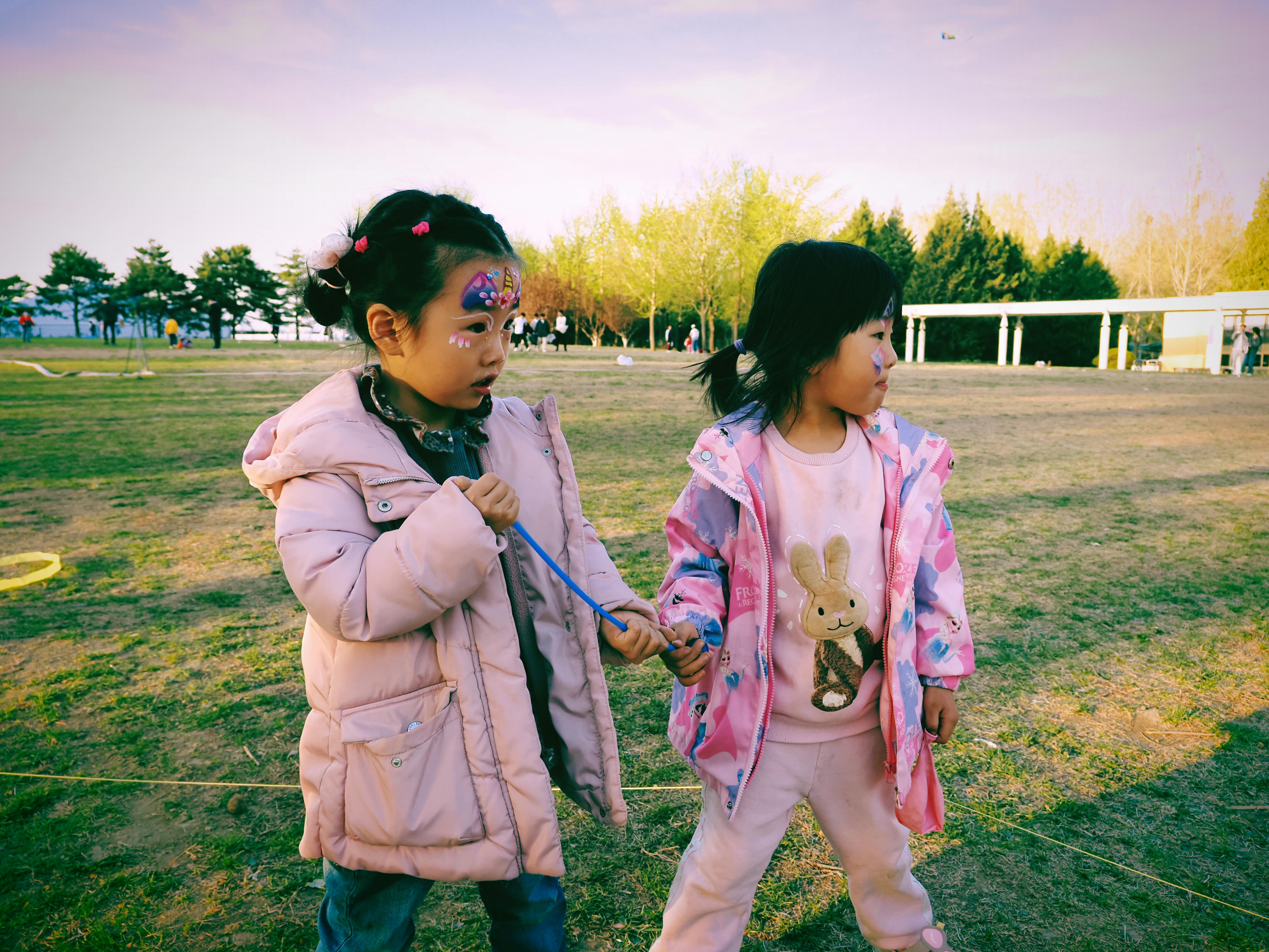 Two young girls with face paintings play outside on a sunny day in the park.