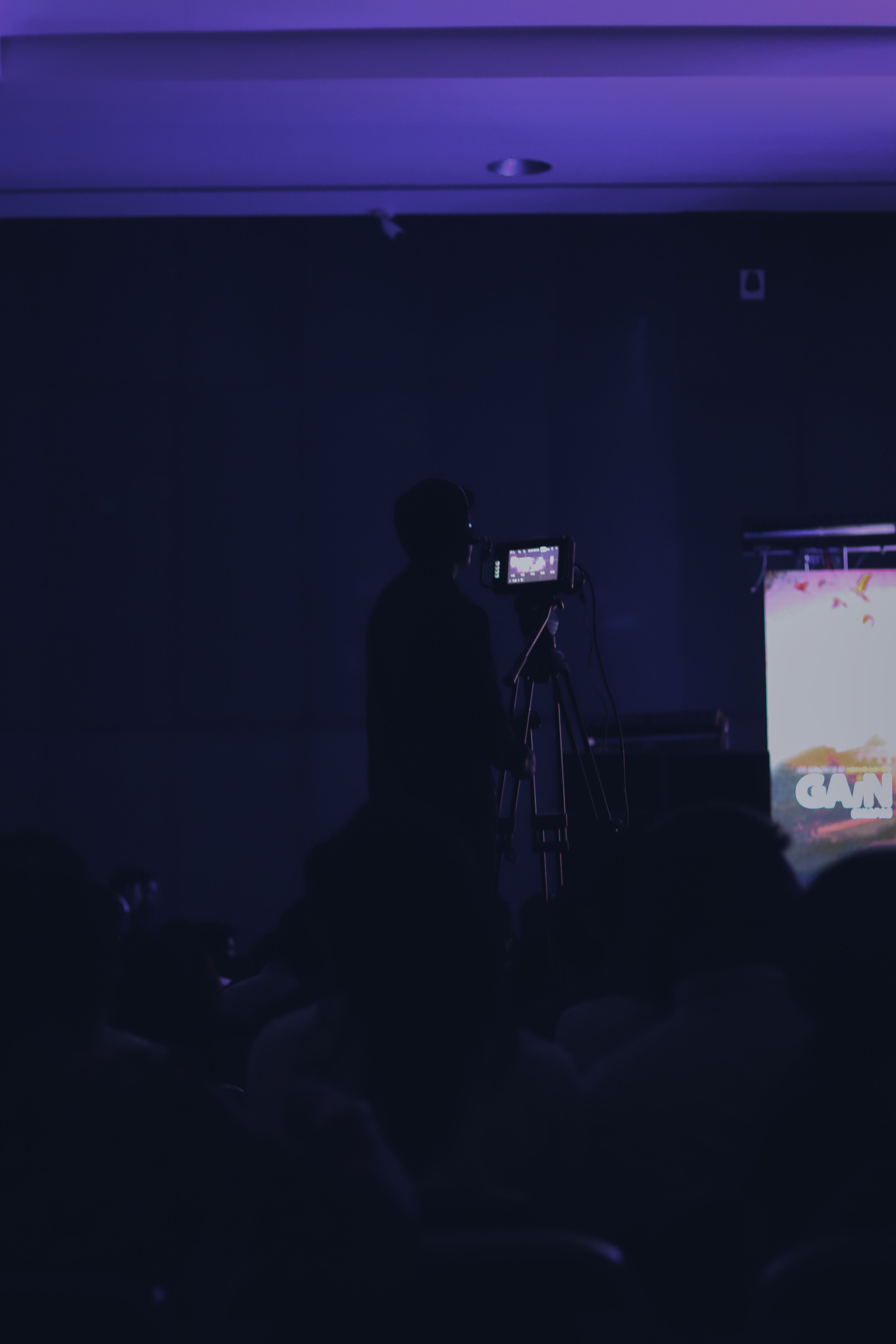 Cameraman silhouette captures event in dimly lit theater ambiance.