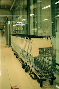 A neatly aligned row of luggage trolleys inside an empty airport terminal with green glass reflections.