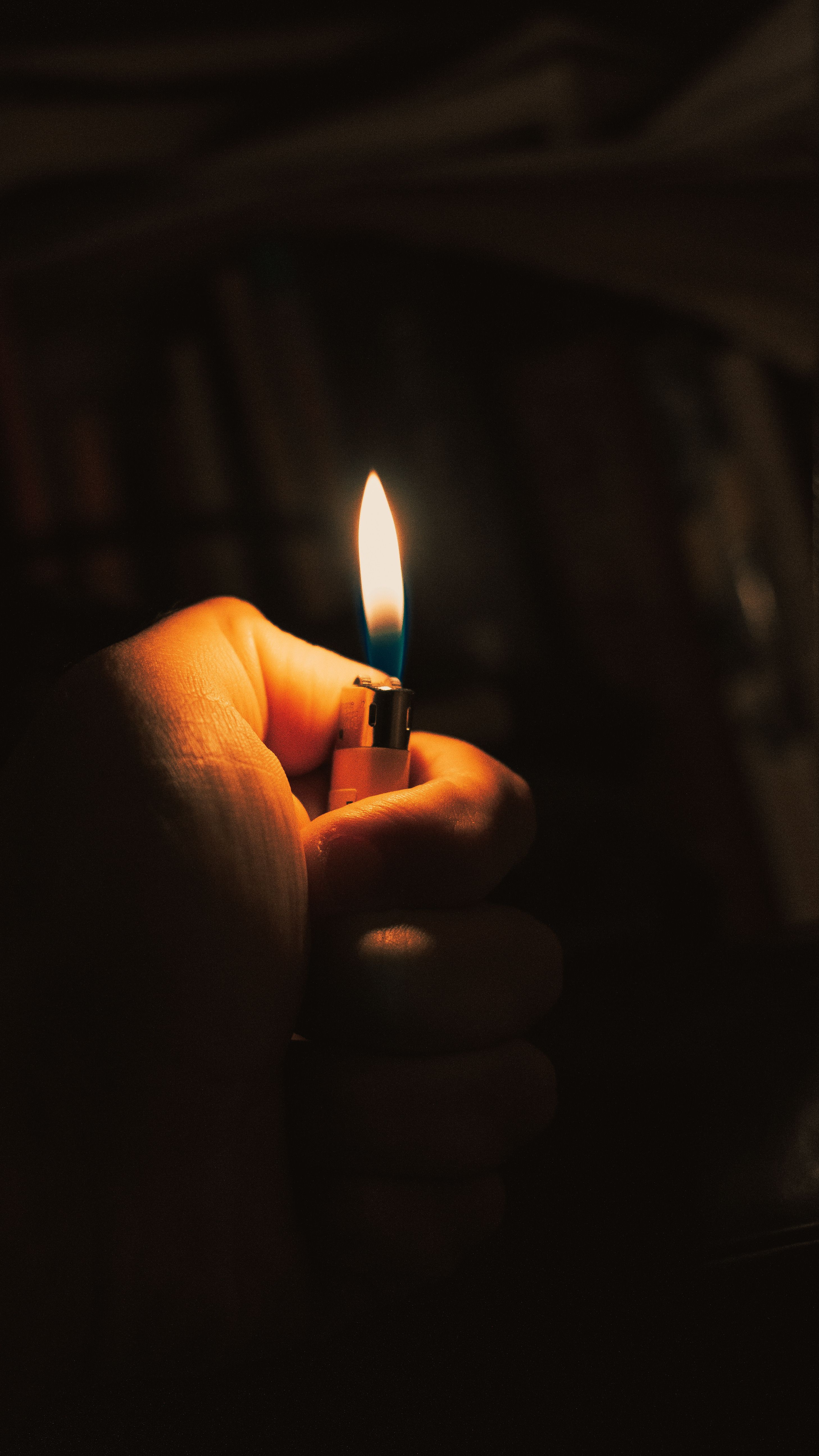 Close-up of a hand holding a lit lighter with a dark background, creating a dramatic scene.
