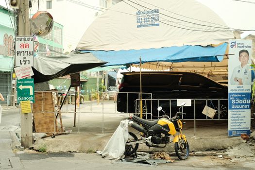 A yellow motorcycle parked beside city street signs and a car under a tent.