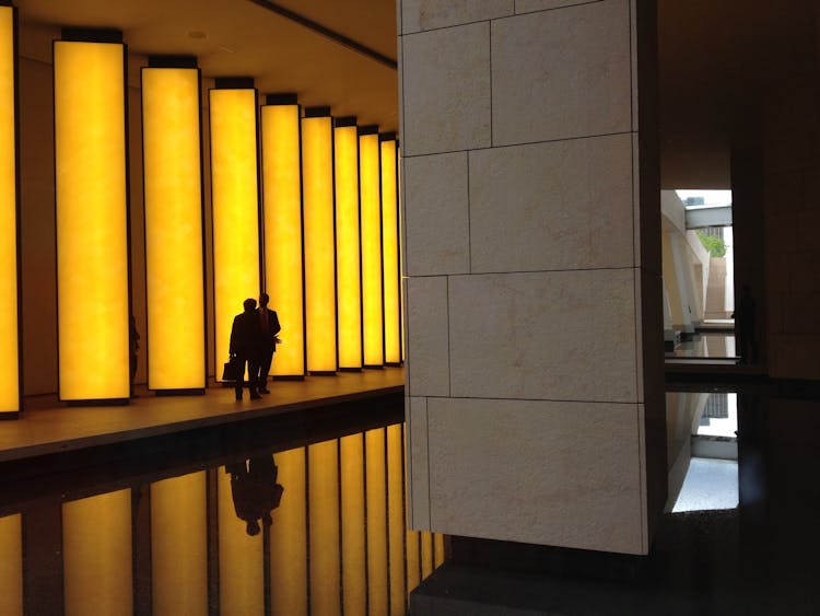 Silhouette Photo Of 2 Person Beside Beige Concrete Lighted Wall