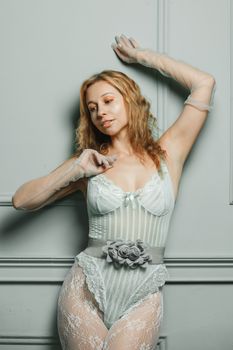Blonde woman posing elegantly in lace lingerie against an interior wall.