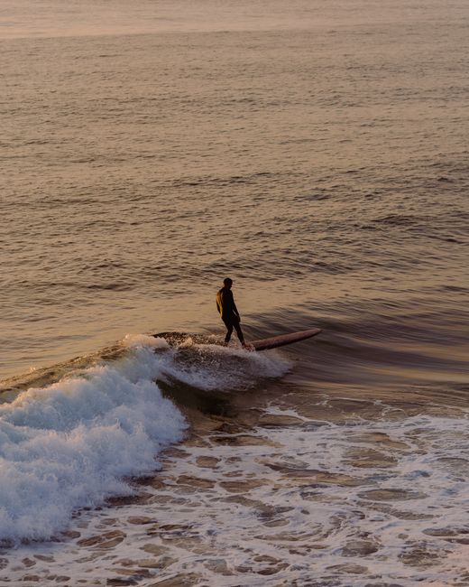 A surfer gracefully rides a wave at sunset in Newport Beach, California.