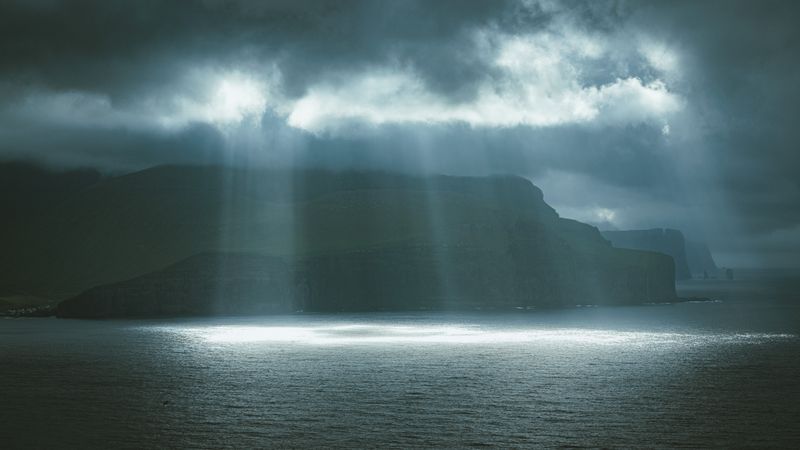 Raze de soare prin nori dramatici deasupra stâncilor din Insulele Feroe