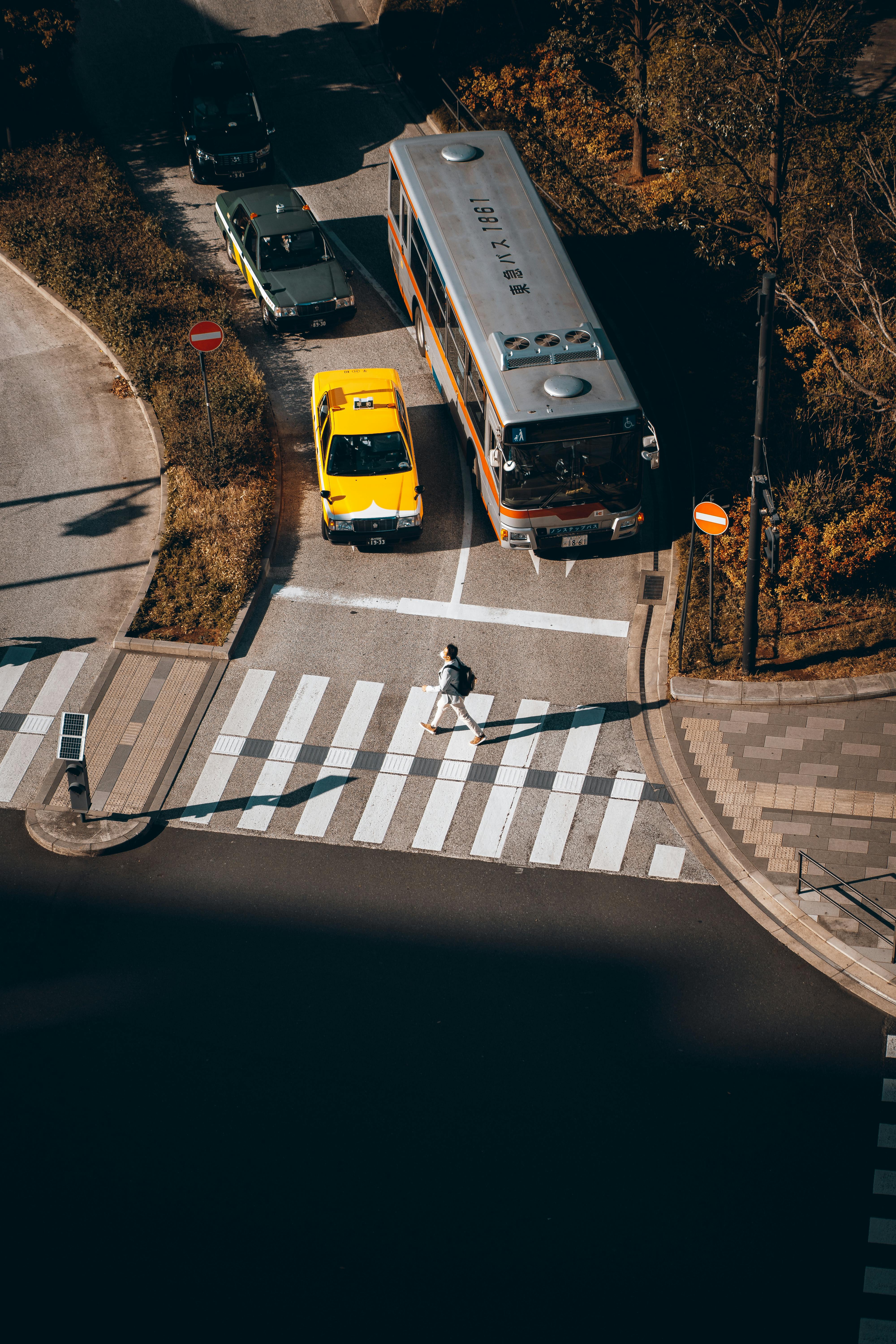An aerial view capturing a busy crosswalk in Tokyo with cars and a pedestrian under sunlight.
