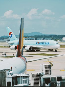 Two Korean Air planes on the tarmac at Incheon Airport under a clear blue sky.