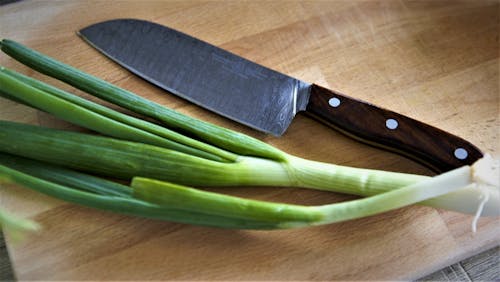 A Sharp Knife Lying next to Spring Onion on a Cutting Board 