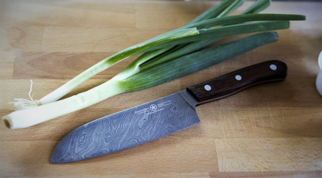 Close-up of a chef's knife and spring onions on a wooden cutting board.