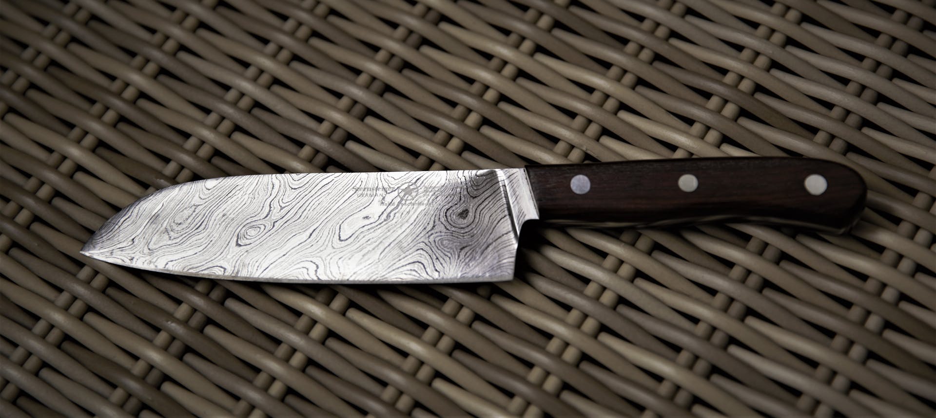 Close-up of a Damascus steel chef knife resting on a wicker surface, showcasing intricate patterns.