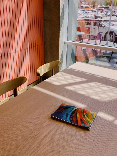 Free A vibrant magazine on a sunlit café table near a window with shadows casting unique patterns. Stock Photo
