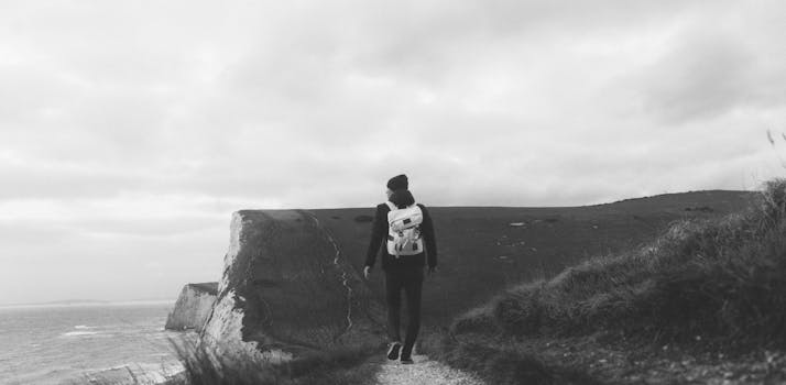 一名孤独的背包客沿着崎岖的悬崖小路，在多云的天空下行走