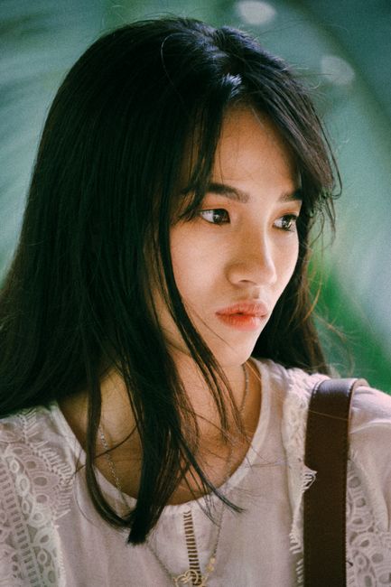Close-up portrait of a young Asian woman with thoughtful expression outdoors.