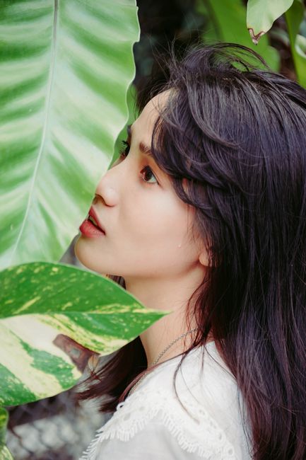 Side profile of a woman surrounded by lush tropical leaves.