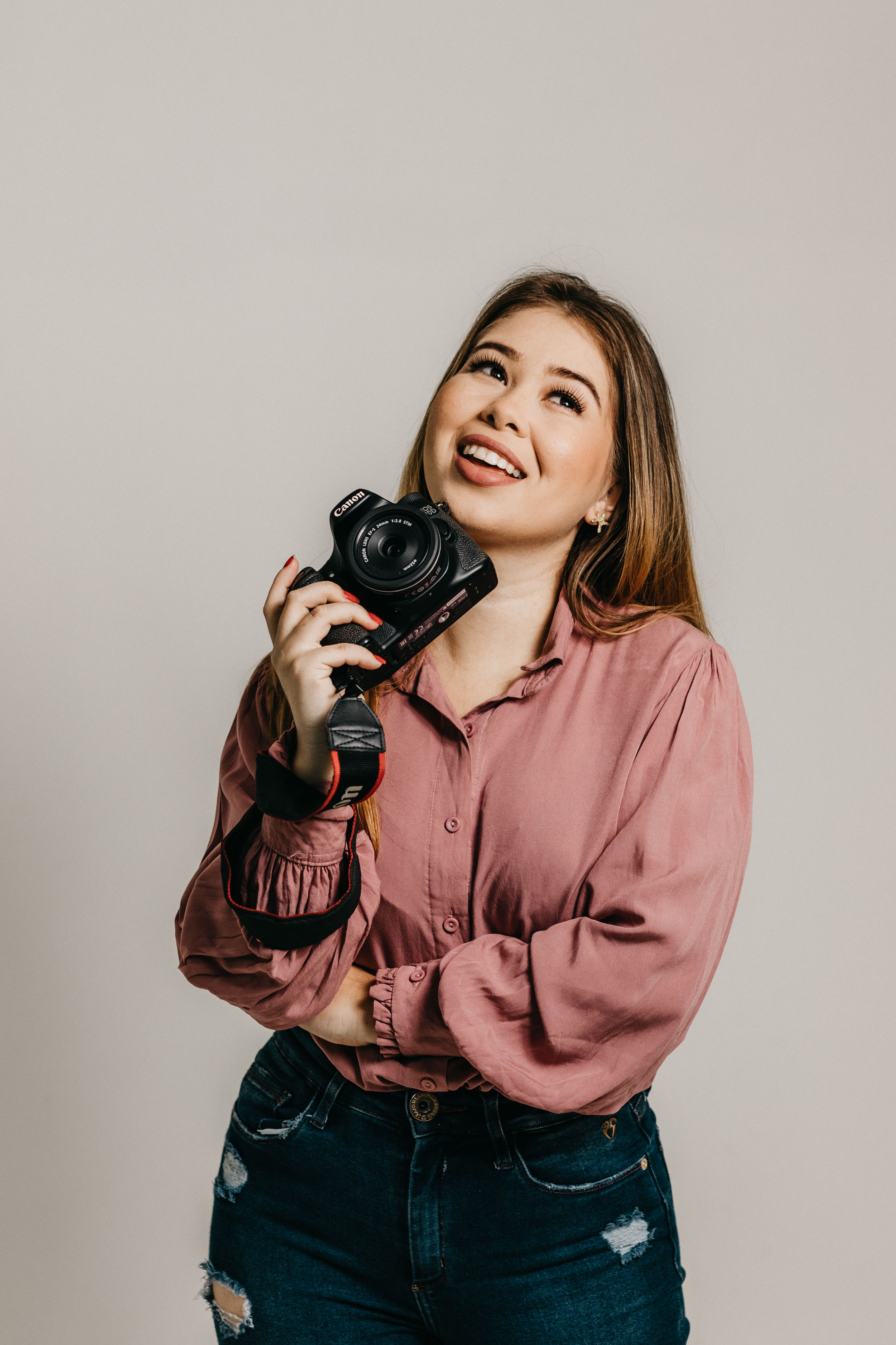 Cheerful brunette woman holding a camera, posing in a studio setting.