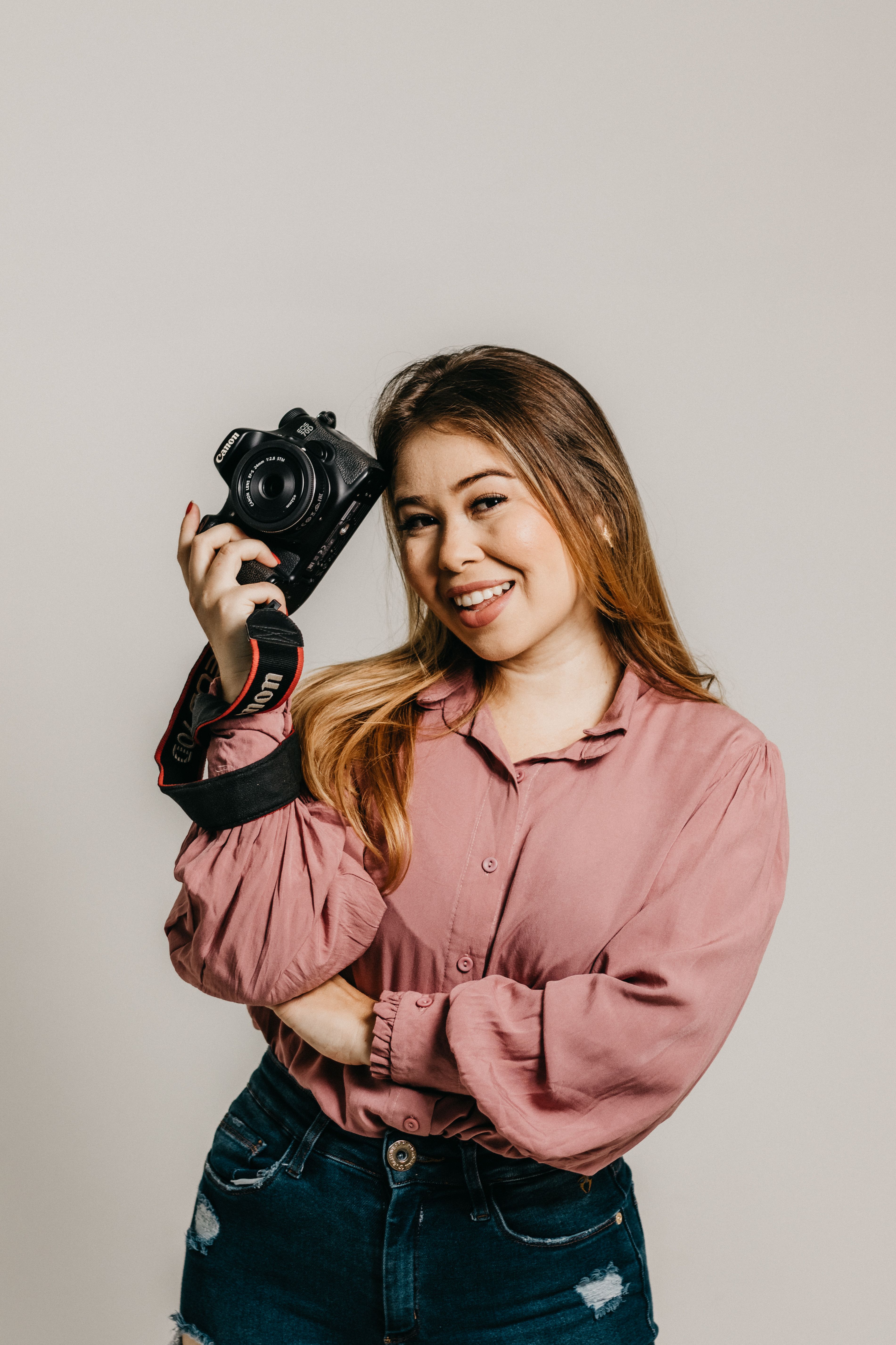 A cheerful young woman holding a camera in a studio setting, showcasing her passion for photography.