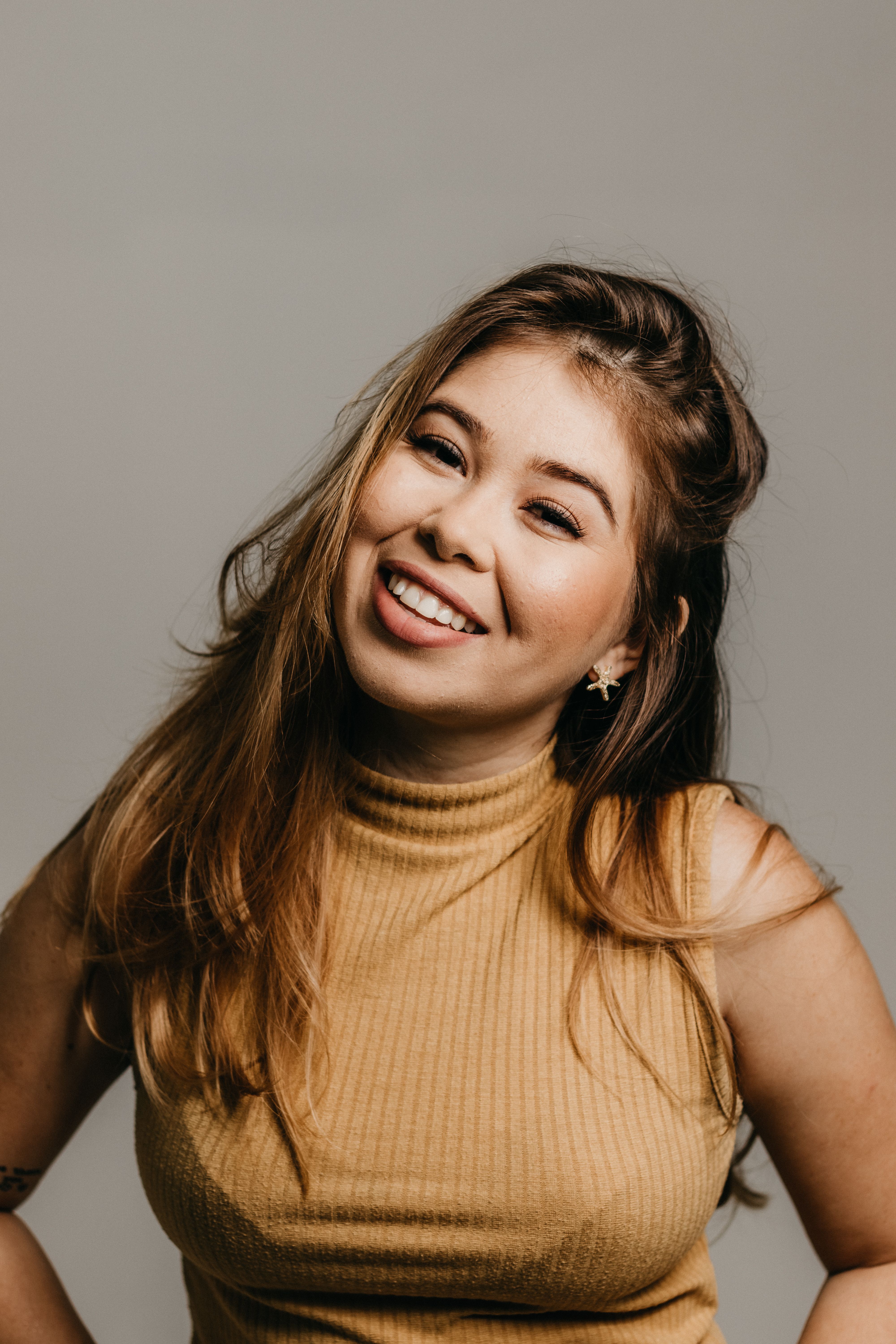 Portrait of a smiling woman in a beige top with long hair in a studio setting.