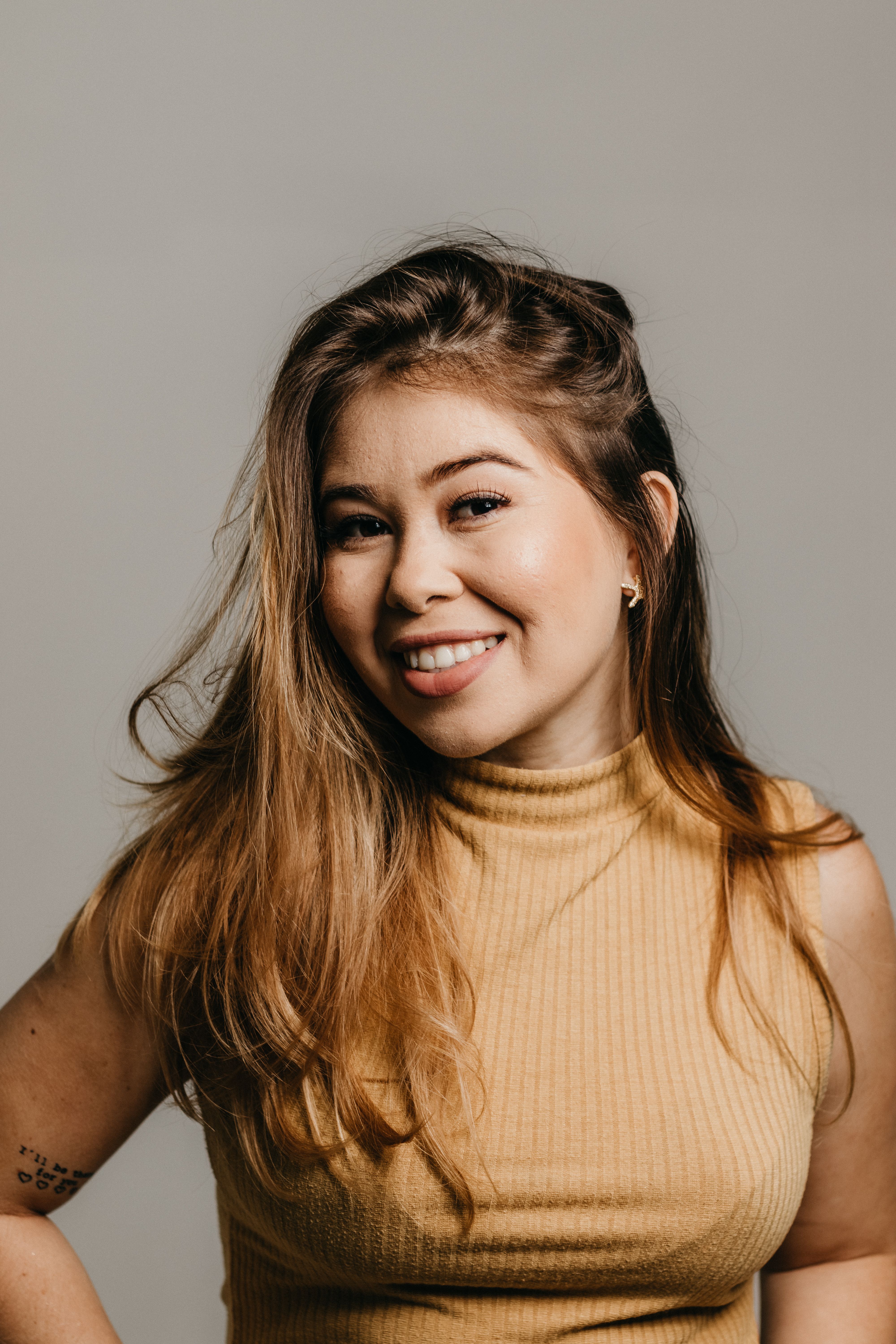 A woman with long hair smiling confidently in a studio portrait.