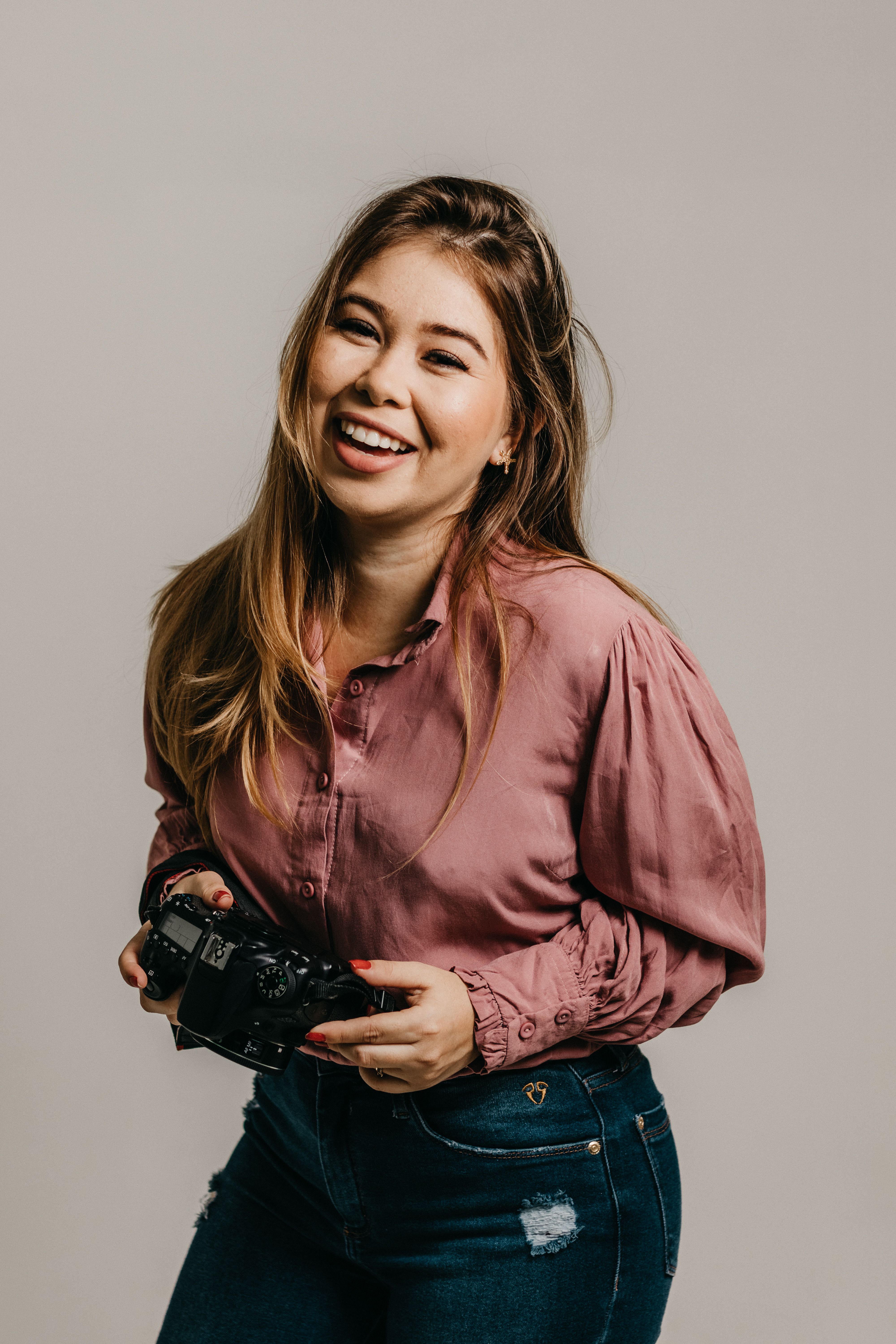Asian woman in a blouse holding a camera and smiling during a studio photoshoot.