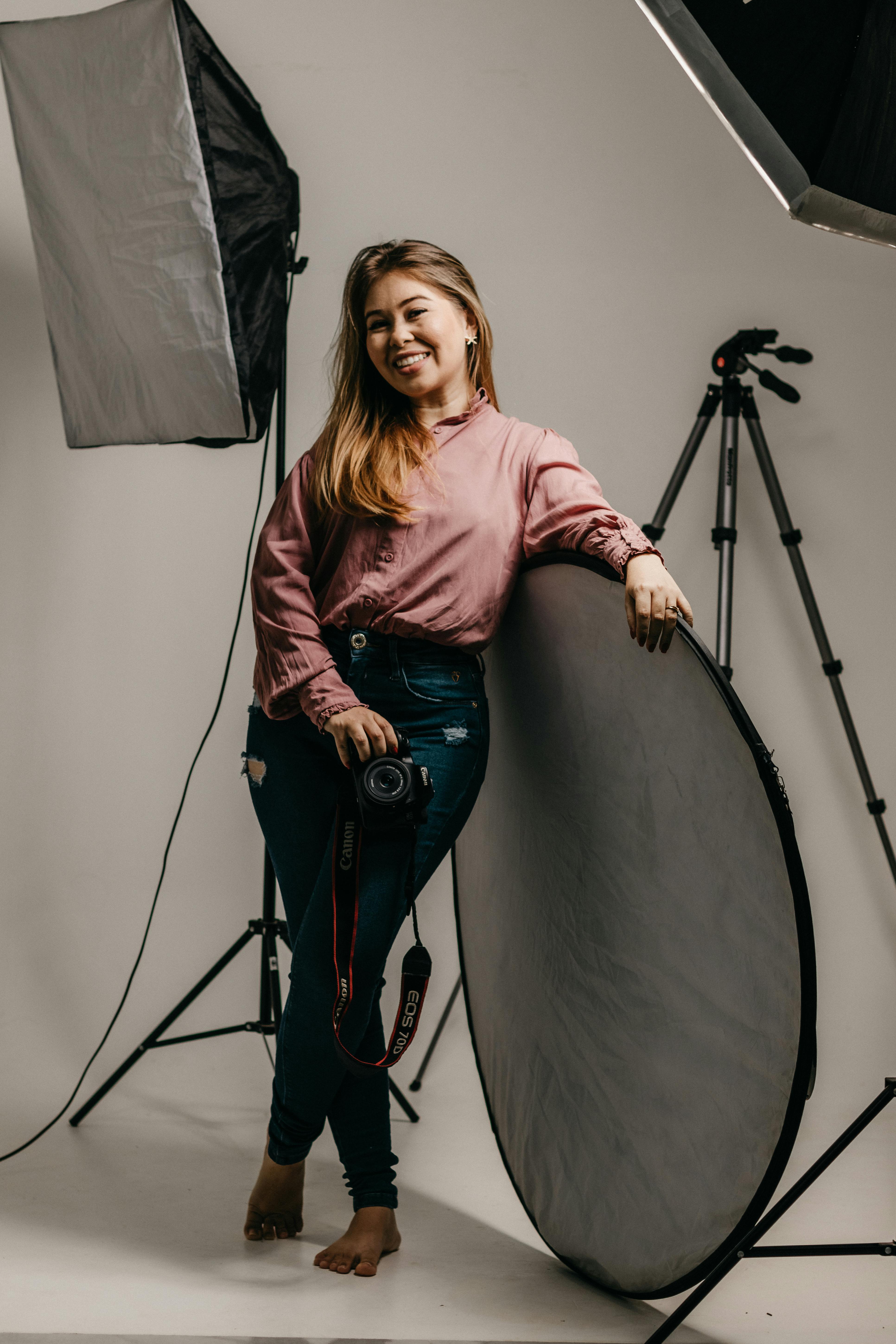 Portrait of an Asian woman photographer holding a camera in a studio setting.