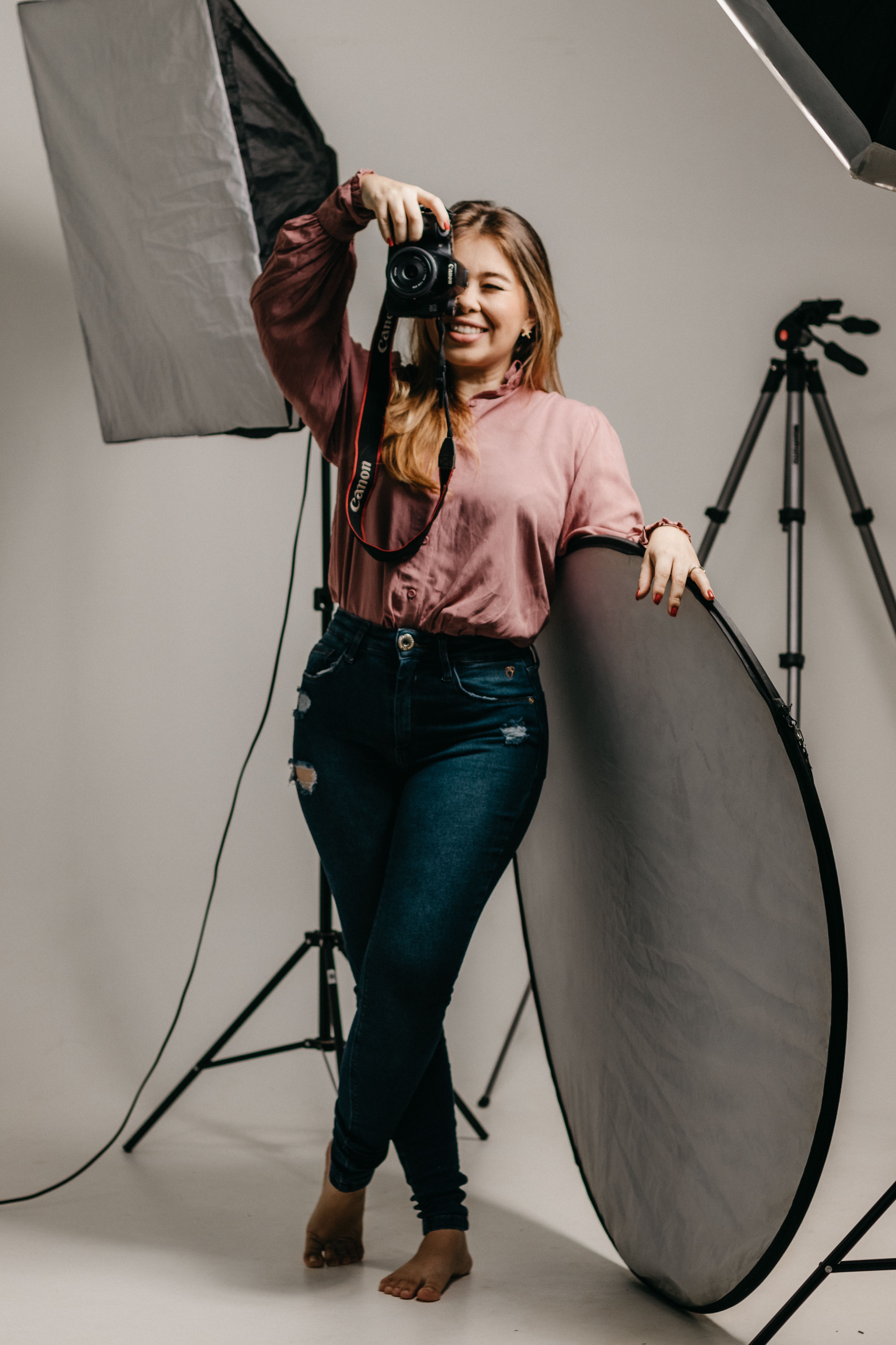 Female photographer smiling and holding a camera in a professional studio setup.
