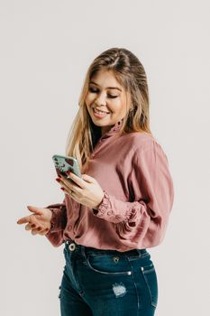 Asian woman in a pink blouse smiling at smartphone in a studio setting.