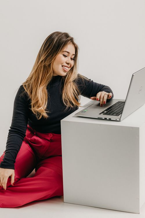 Free Asian woman with laptop in studio, wearing red pants and black top, smiling. Stock Photo