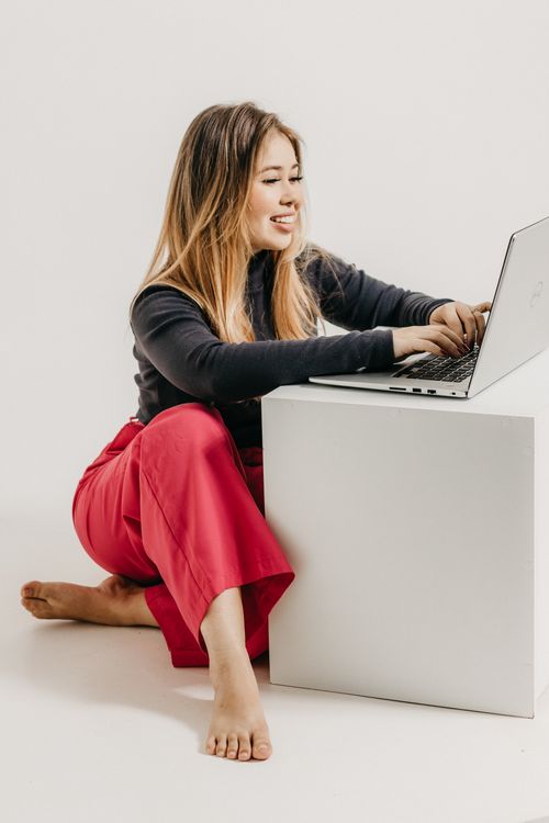 Free A woman in red trousers and black top uses a laptop on a white surface in a studio setting. Stock Photo