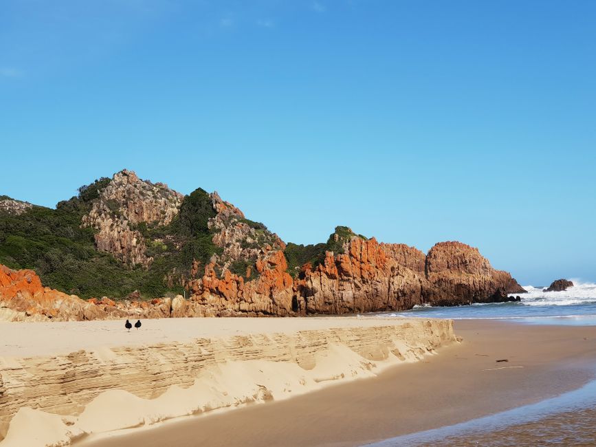 Explore a stunning beach with orange rocky cliffs under a clear blue sky.