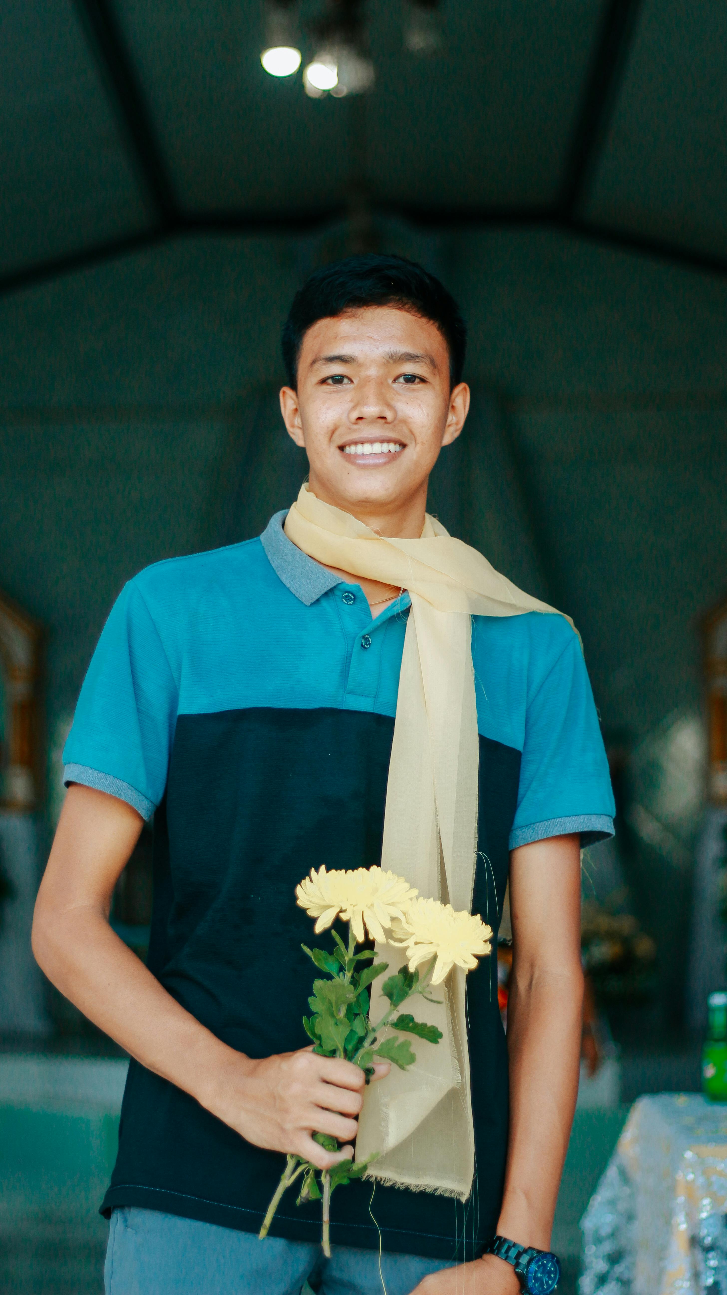 Young man in a casual outfit holding yellow flowers and smiling indoors.