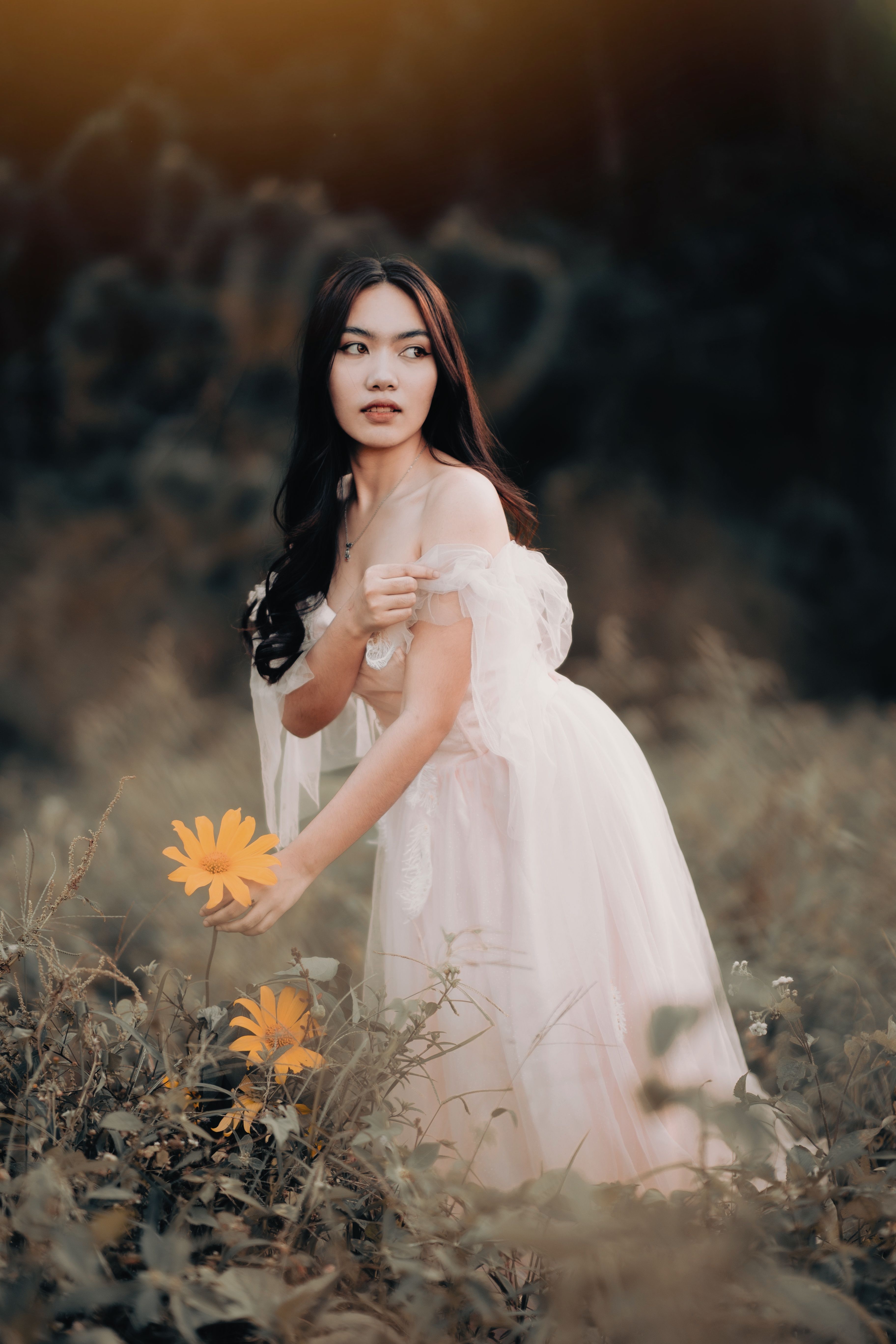 Asian woman in wedding dress holding flowers in a romantic outdoor setting.