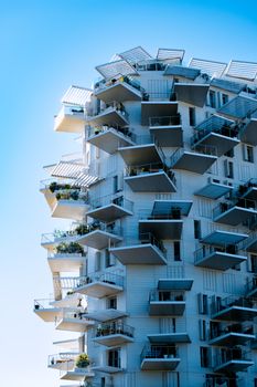Low-angle view of a modern building with geometric balconies against a clear blue sky.
