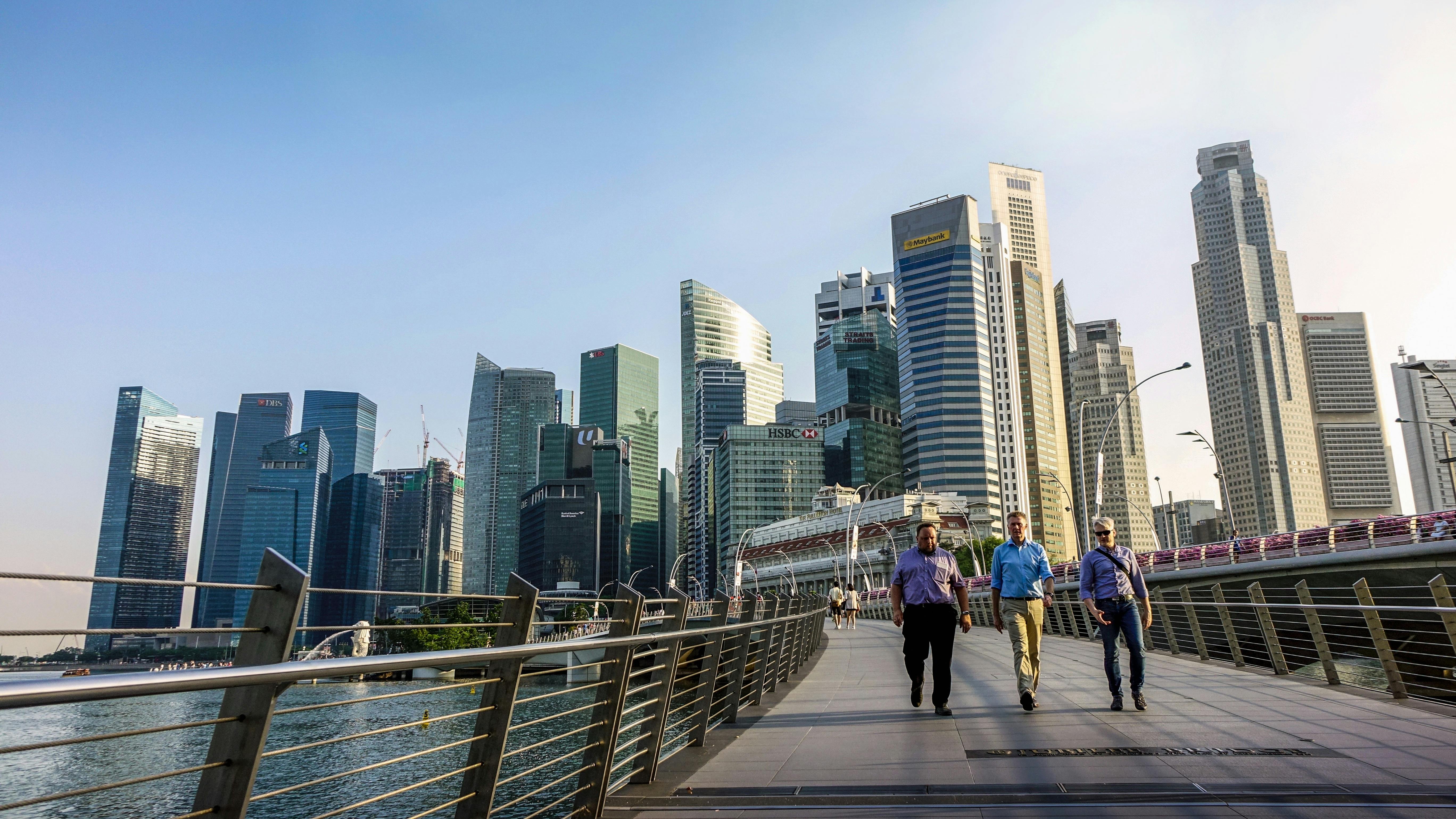 three men walking on bridge in front of high rise buildings at daytime