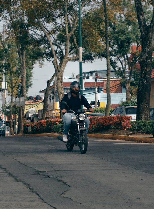 Free A motorcyclist rides through an urban street lined with trees and colorful houses during the day. Stock Photo