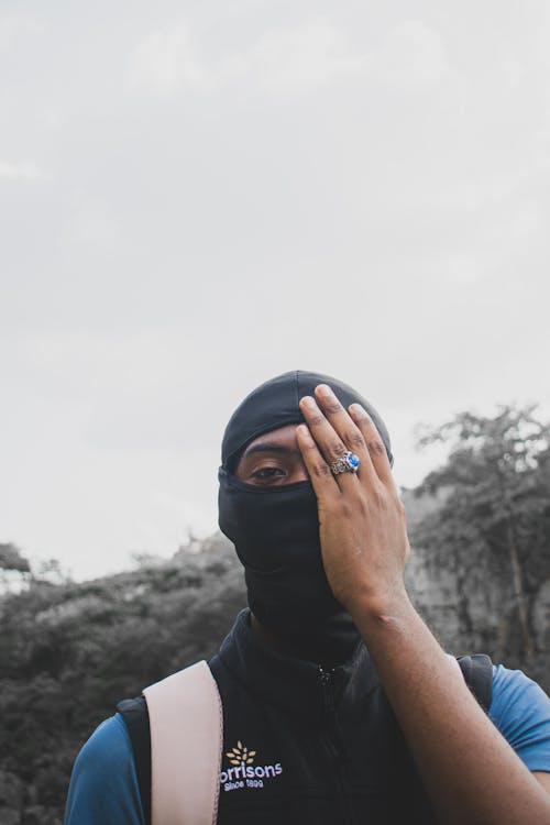 Man in a Black Balaclava Standing and Covering His Eye 
